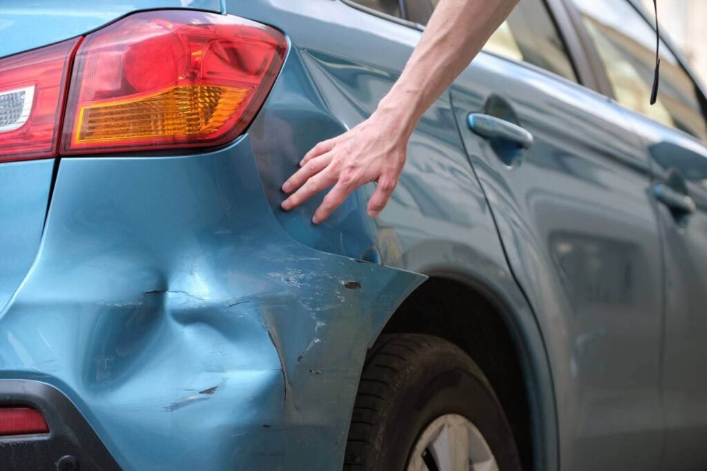 Driver looking at dent located at the back of their car
